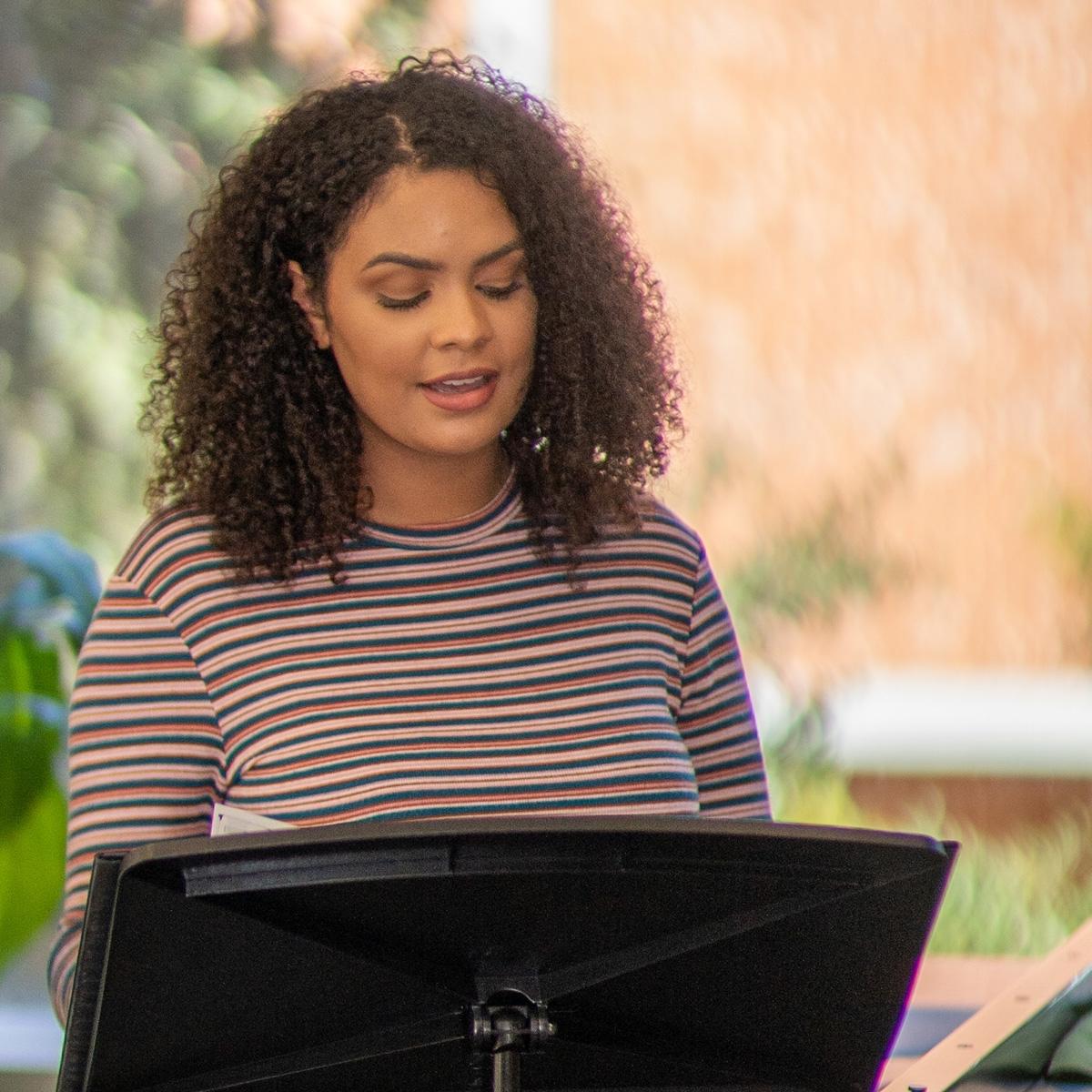 Caelia Marshall sings with sheet music on a music stand in a faculty rehearsal space